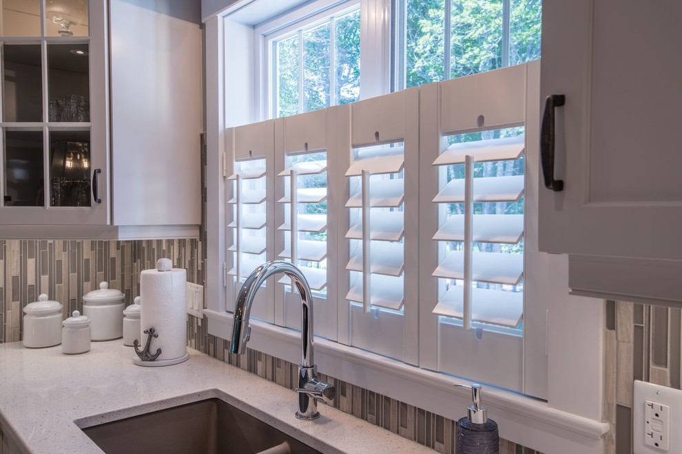 Photo of a medium sized nautical l-shaped enclosed kitchen in Other with a double-bowl sink, shaker cabinets, white cabinets, engineered stone countertops, beige splashback, matchstick tiled splashback and stainless steel appliances.