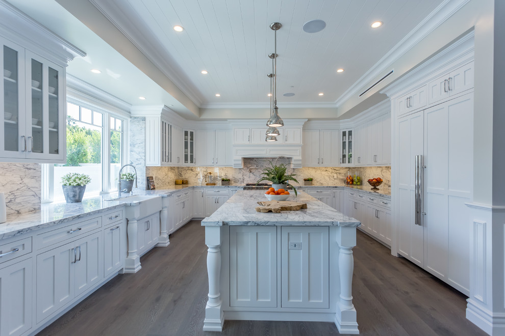 Photo of an expansive classic u-shaped open plan kitchen in Los Angeles with a belfast sink, white cabinets, marble worktops, stone slab splashback, stainless steel appliances, light hardwood flooring and an island.