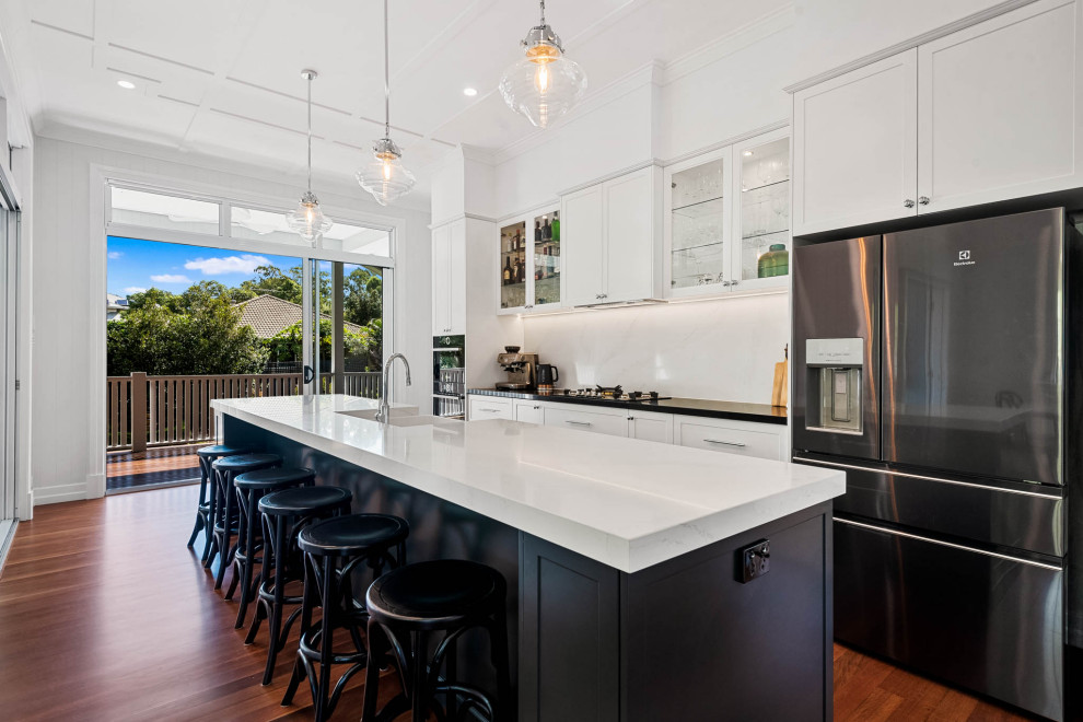 Zweizeilige Klassische Küche mit Landhausspüle, Schrankfronten im Shaker-Stil, Küchenrückwand in Weiß, Küchengeräten aus Edelstahl, braunem Holzboden, Kücheninsel, braunem Boden und weißer Arbeitsplatte in Brisbane