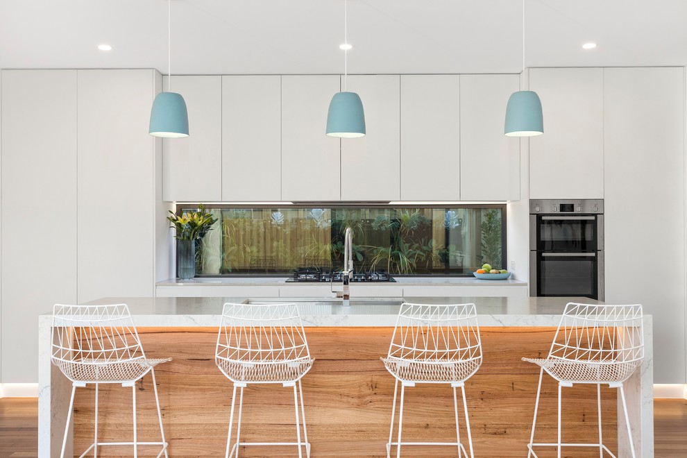 Large contemporary galley kitchen/diner in Geelong with stainless steel appliances, medium hardwood flooring, an island, brown floors, white worktops, a submerged sink, flat-panel cabinets, white cabinets and window splashback.