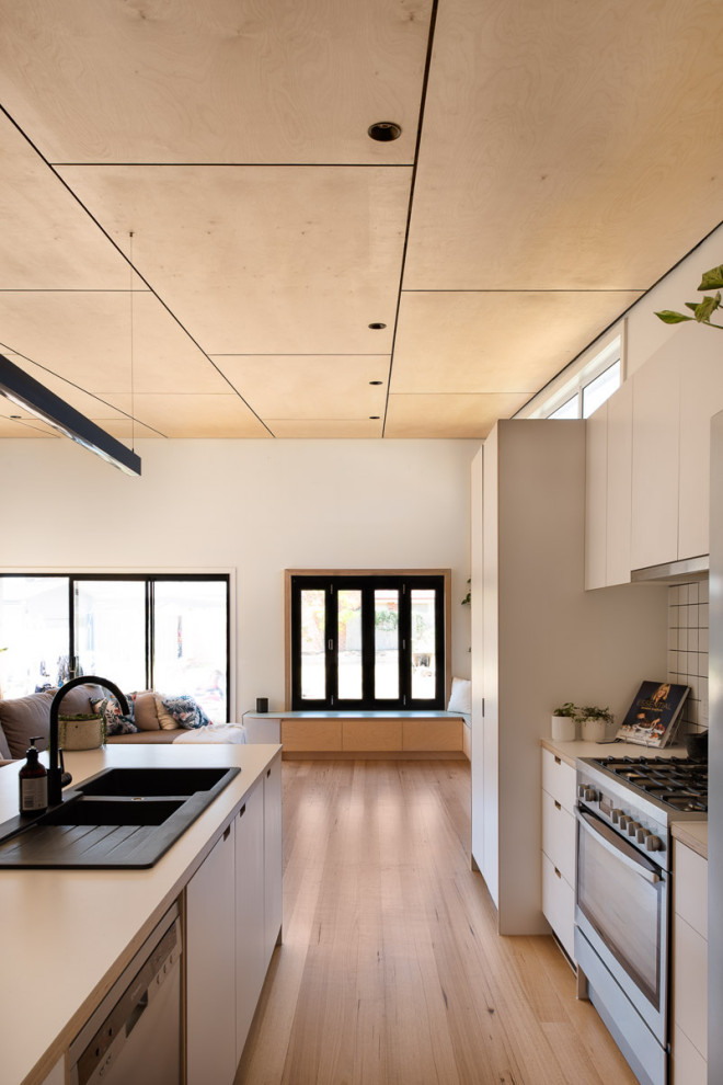 Cette image montre une grande cuisine ouverte minimaliste avec des portes de placard blanches, une crédence blanche, une crédence en céramique, un électroménager en acier inoxydable, îlot et un plan de travail beige.