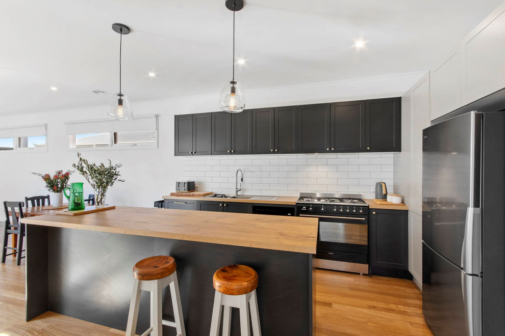Eat-in kitchen - mid-sized contemporary medium tone wood floor eat-in kitchen idea in Geelong with a double-bowl sink, shaker cabinets, wood countertops, white backsplash, ceramic backsplash, black appliances, an island and brown countertops