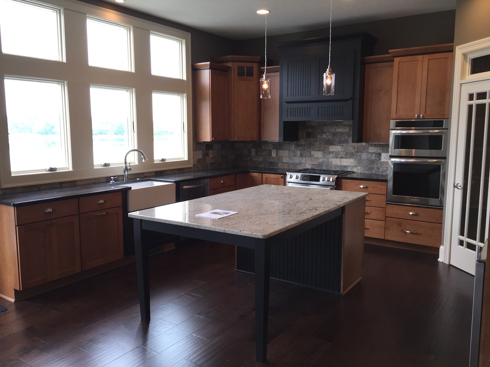 Large traditional l-shaped kitchen/diner in Indianapolis with a belfast sink, recessed-panel cabinets, medium wood cabinets, granite worktops, metallic splashback, ceramic splashback, stainless steel appliances, dark hardwood flooring and an island.