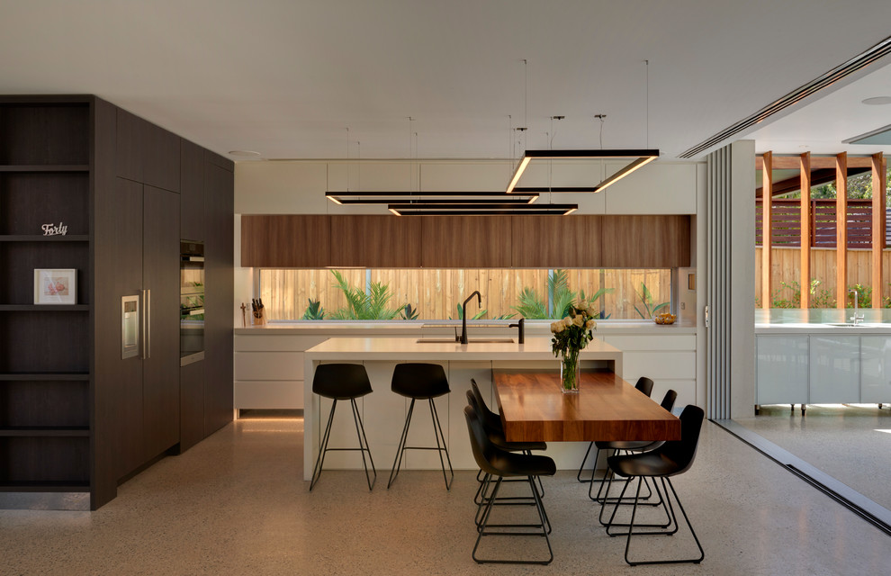 Exempel på ett stort modernt linjärt kök och matrum, med betonggolv, en dubbel diskho, rostfria vitvaror, bänkskiva i kvarts, släta luckor, vita skåp, fönster som stänkskydd och en köksö