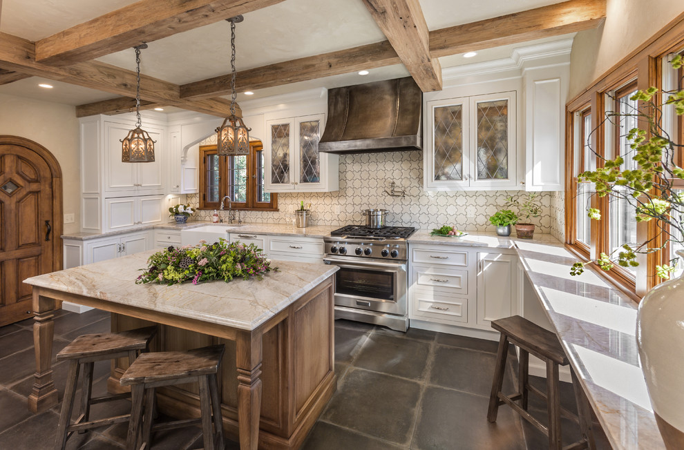 Kitchen - mid-sized traditional u-shaped brown floor kitchen idea in Milwaukee with a farmhouse sink, glass-front cabinets, white cabinets, marble countertops, ceramic backsplash, stainless steel appliances, an island and multicolored backsplash