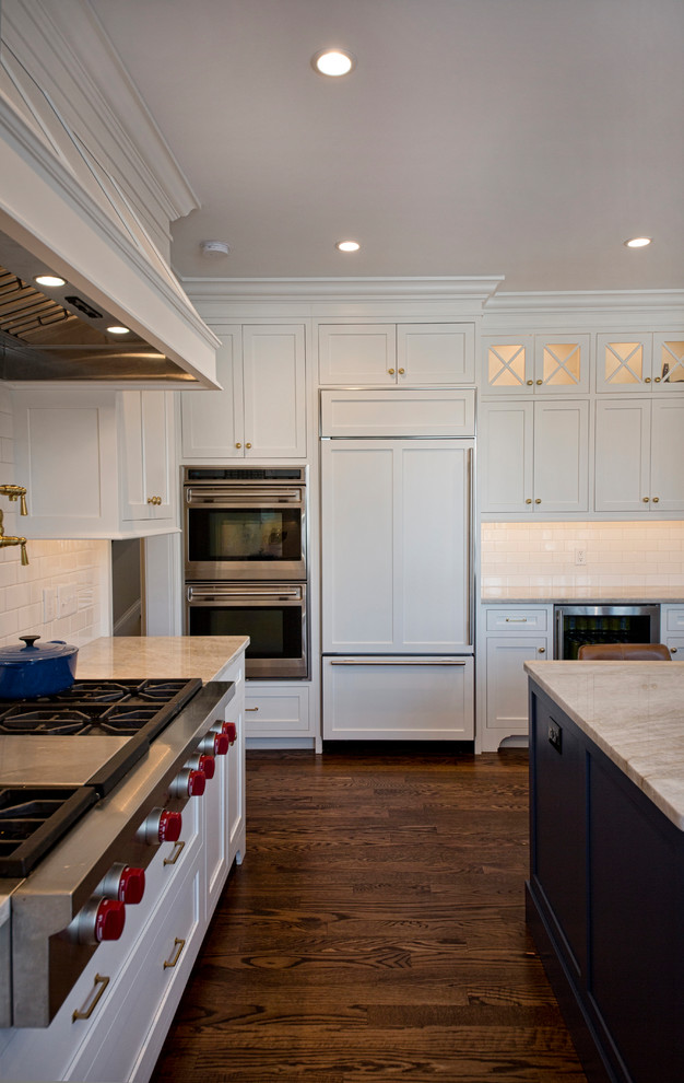Eat-in kitchen - transitional l-shaped medium tone wood floor and brown floor eat-in kitchen idea in Cleveland with a farmhouse sink, shaker cabinets, white backsplash, subway tile backsplash, paneled appliances, an island, white cabinets, granite countertops and white countertops