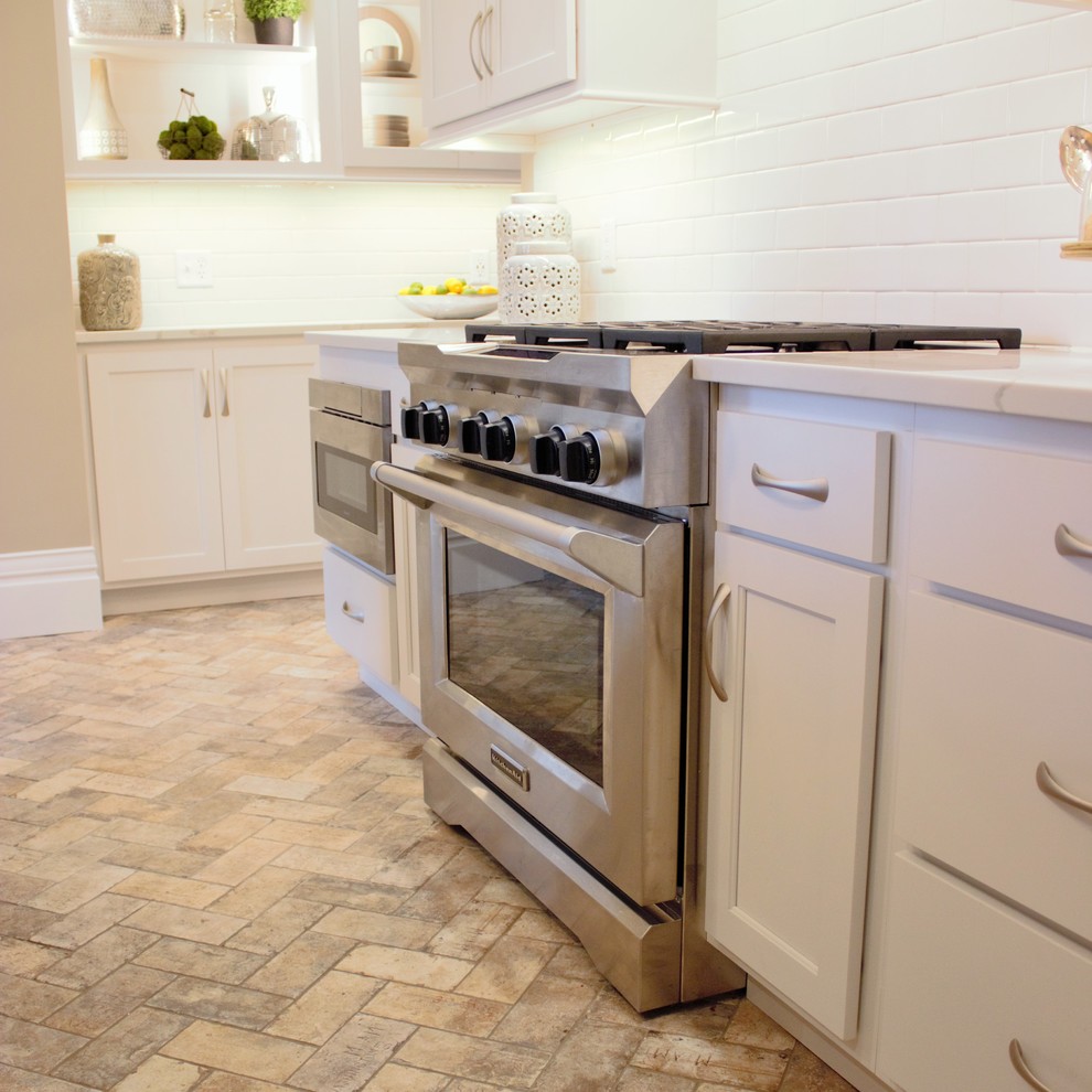 Exempel på ett avskilt, mellanstort klassiskt kök, med en rustik diskho, släta luckor, vita skåp, bänkskiva i kvarts, vitt stänkskydd, stänkskydd i tunnelbanekakel, rostfria vitvaror, tegelgolv, en köksö och beiget golv