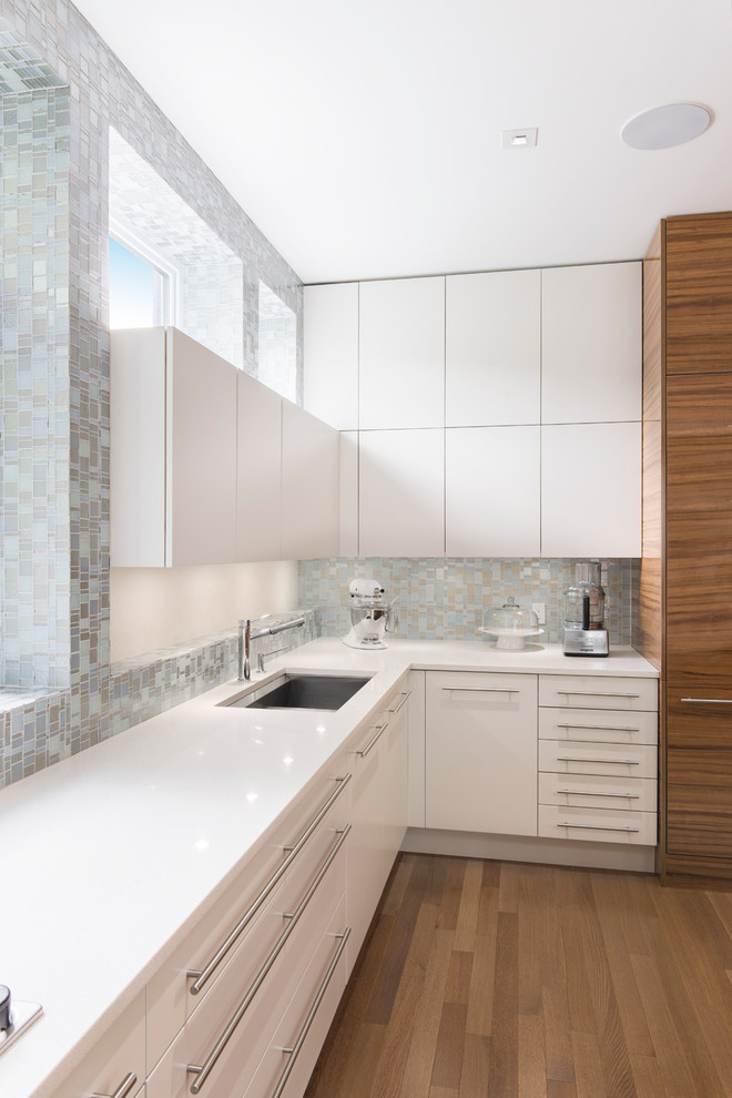 Foto di una cucina a L minimal con lavello sottopiano, ante lisce, ante bianche, paraspruzzi grigio, paraspruzzi con piastrelle a mosaico e pavimento in legno massello medio
