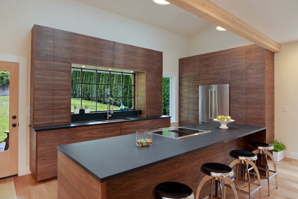 Immagine di un cucina con isola centrale contemporaneo con lavello sottopiano, ante lisce, ante in legno scuro, elettrodomestici in acciaio inossidabile e parquet chiaro