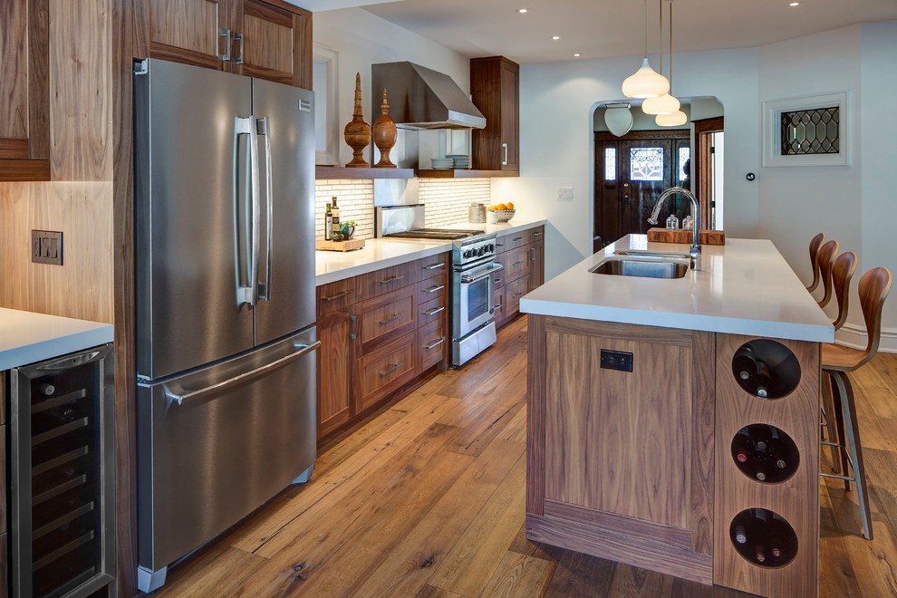 Example of a mid-sized transitional galley medium tone wood floor open concept kitchen design in Toronto with a double-bowl sink, shaker cabinets, medium tone wood cabinets, white backsplash, ceramic backsplash and stainless steel appliances