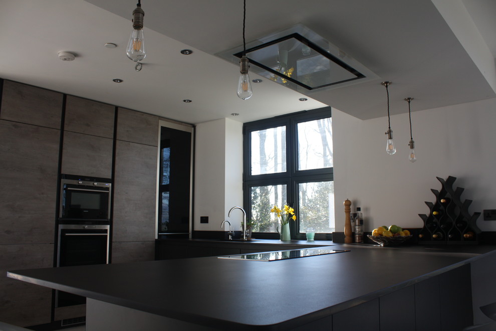Modern inredning av ett mellanstort grå grått kök, med en halv köksö, en undermonterad diskho, släta luckor, grå skåp, bänkskiva i koppar, grått stänkskydd, svarta vitvaror, klinkergolv i keramik och grått golv