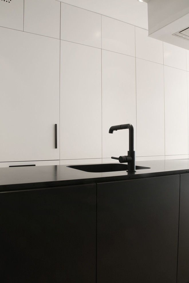 Ispirazione per una cucina moderna di medie dimensioni con lavello sottopiano, ante lisce, ante nere, top in superficie solida, elettrodomestici da incasso, parquet chiaro e pavimento beige