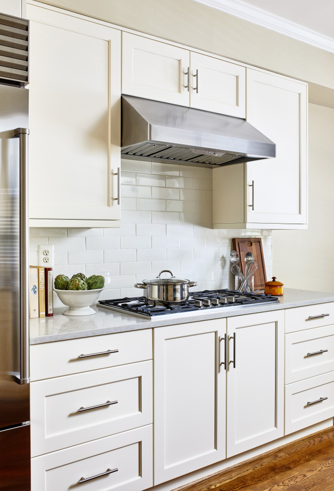 ワシントンD.C.にある中くらいなトランジショナルスタイルのおしゃれなキッチン (アンダーカウンターシンク、シェーカースタイル扉のキャビネット、白いキャビネット、珪岩カウンター、白いキッチンパネル、サブウェイタイルのキッチンパネル、シルバーの調理設備、無垢フローリング、茶色い床、グレーのキッチンカウンター) の写真