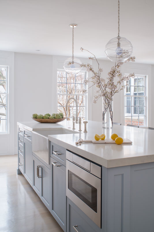 Klassisk inredning av ett stort grå linjärt grått kök och matrum, med en rustik diskho, släta luckor, blå skåp, bänkskiva i kvarts, vitt stänkskydd, stänkskydd i mosaik, rostfria vitvaror, laminatgolv, en köksö och beiget golv