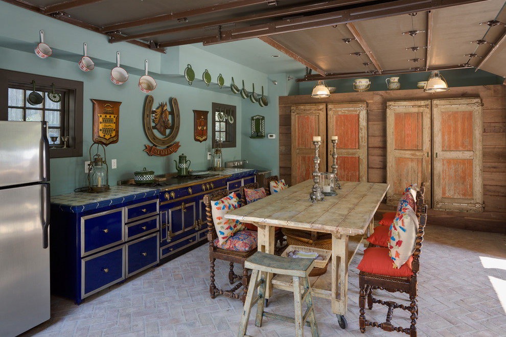 Пример оригинального дизайна: кухня в стиле фьюжн с обеденным столом, синими фасадами, цветной техникой и кирпичным полом