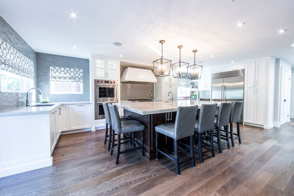 Inspiration for a large transitional u-shaped medium tone wood floor and brown floor open concept kitchen remodel in Toronto with an undermount sink, shaker cabinets, white cabinets, onyx countertops, beige backsplash, glass tile backsplash, stainless steel appliances, an island and beige countertops