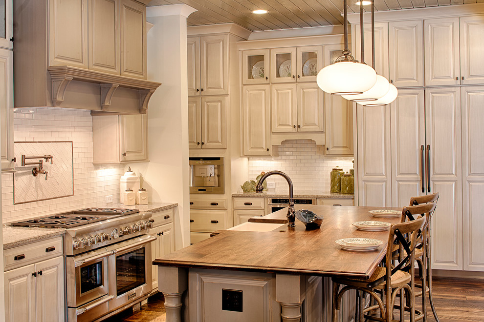 Open concept kitchen - mid-sized traditional l-shaped medium tone wood floor open concept kitchen idea in Charlotte with a farmhouse sink, raised-panel cabinets, distressed cabinets, quartzite countertops, white backsplash, subway tile backsplash, stainless steel appliances and an island
