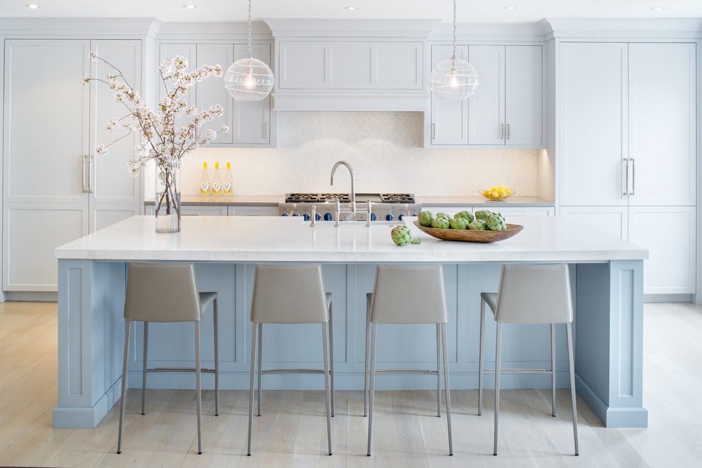 Immagine di una cucina classica con ante con riquadro incassato, ante blu, paraspruzzi bianco, elettrodomestici in acciaio inossidabile, parquet chiaro, pavimento beige e top bianco