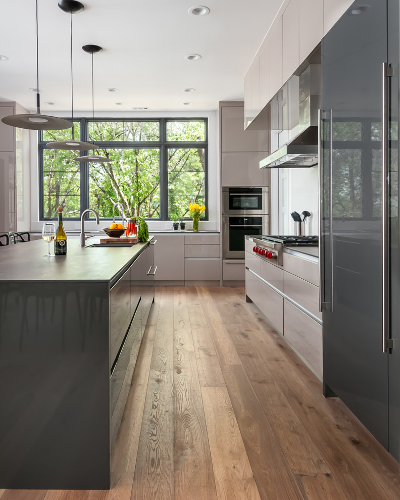 Trendy l-shaped medium tone wood floor and brown floor enclosed kitchen photo in Chicago with an undermount sink, flat-panel cabinets, beige cabinets, stainless steel appliances, an island and gray countertops