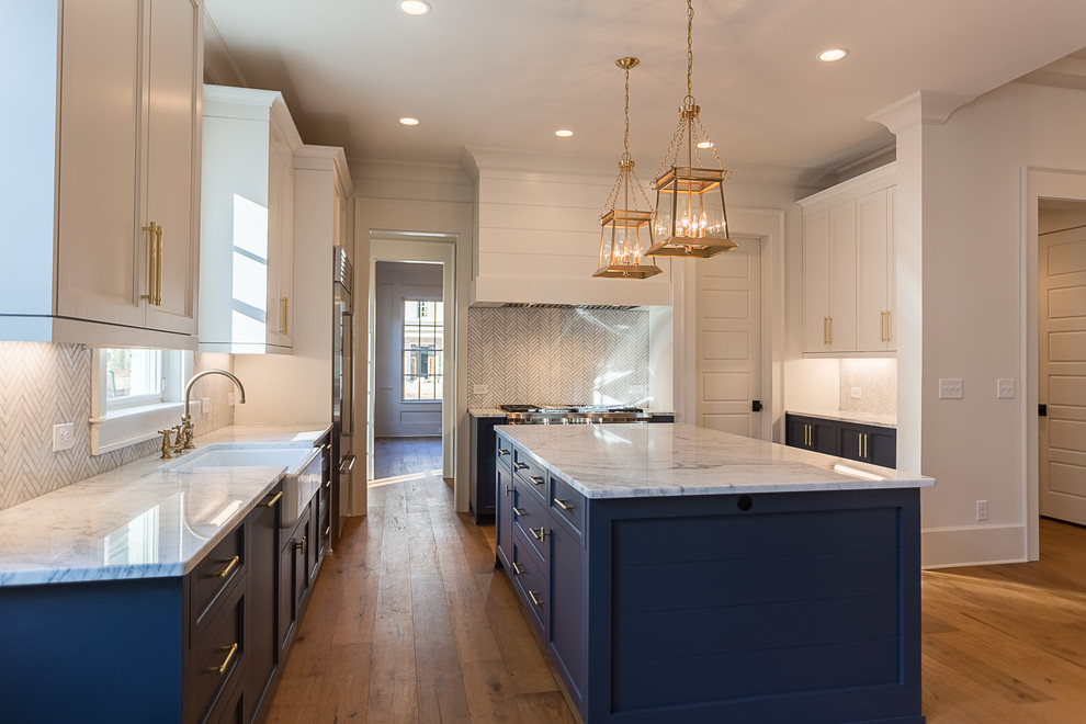 Inspiration for a medium sized traditional l-shaped open plan kitchen in Atlanta with a belfast sink, recessed-panel cabinets, blue cabinets, marble worktops, white splashback, ceramic splashback, stainless steel appliances, medium hardwood flooring, an island and brown floors.