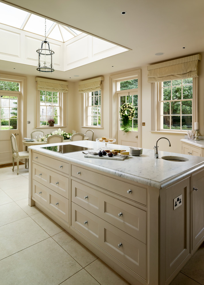 Cette image montre une grande cuisine américaine traditionnelle avec un placard à porte affleurante, îlot, plan de travail en marbre et une crédence grise.