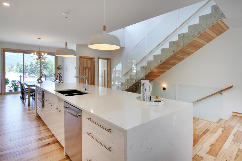 Idéer för att renovera ett mellanstort funkis vit linjärt vitt kök och matrum, med en dubbel diskho, släta luckor, vita skåp, marmorbänkskiva, vitt stänkskydd, stänkskydd i porslinskakel, mellanmörkt trägolv, en köksö och brunt golv