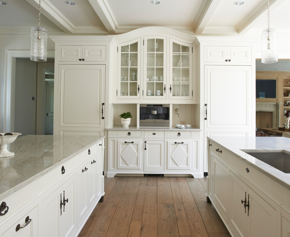 Exempel på ett stort klassiskt kök, med en undermonterad diskho, luckor med upphöjd panel, vita skåp, marmorbänkskiva, beige stänkskydd, stänkskydd i keramik, integrerade vitvaror, ljust trägolv, flera köksöar och vitt golv