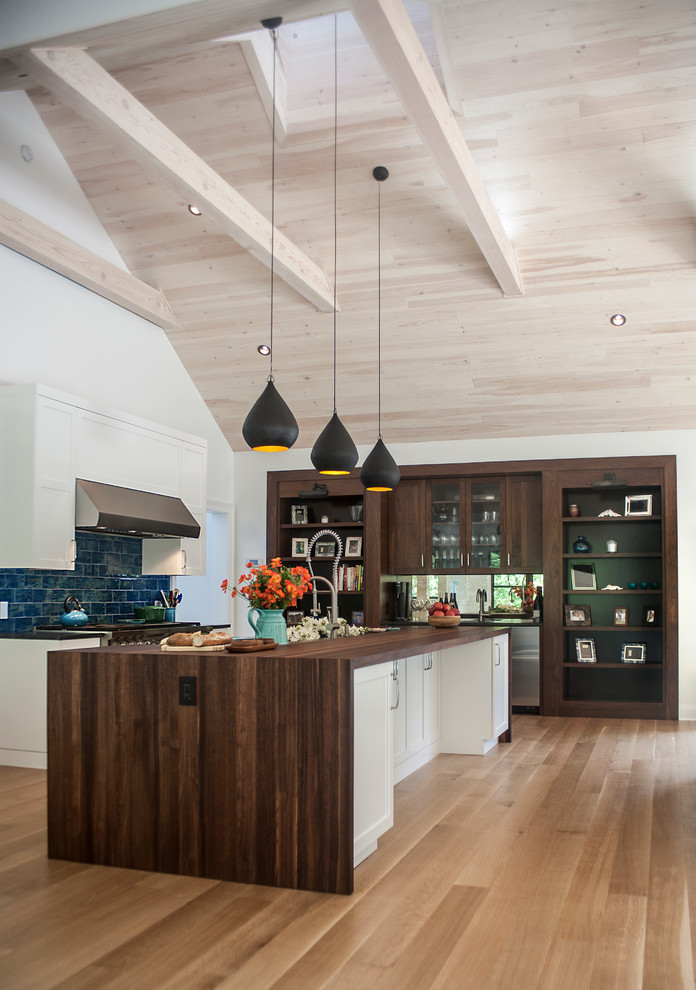 Exemple d'une cuisine ouverte parallèle chic avec un placard avec porte à panneau encastré, des portes de placard blanches, une crédence bleue, une crédence en carrelage métro, un électroménager en acier inoxydable et un sol en bois brun.