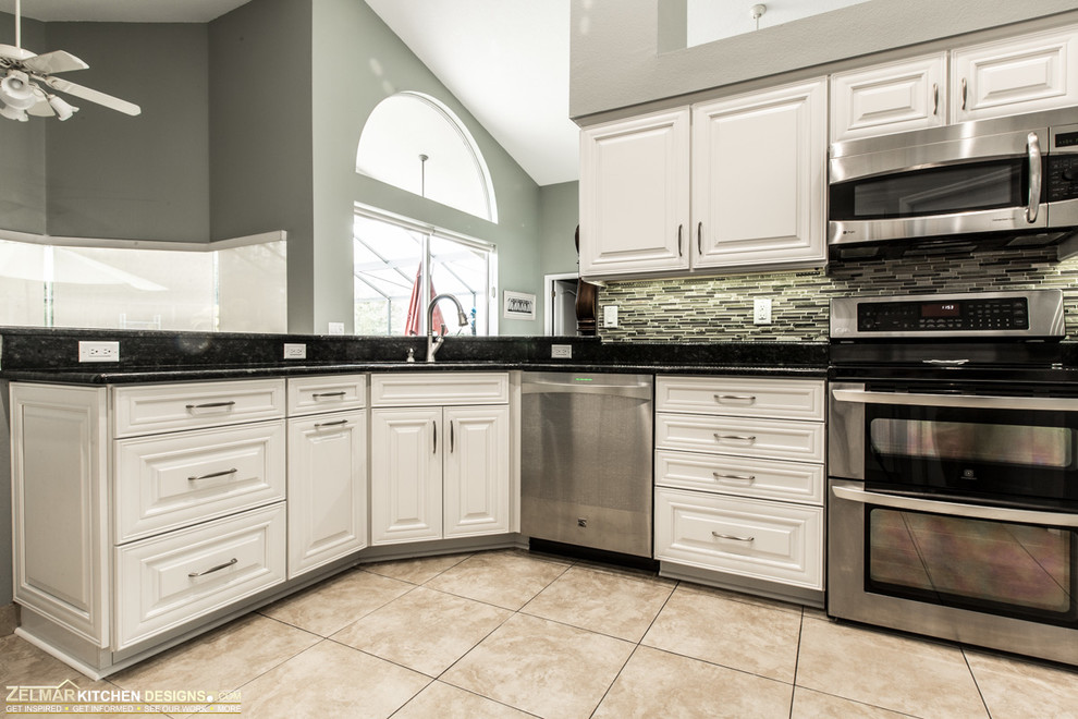 This is an example of a large classic u-shaped kitchen pantry in Orlando with a submerged sink, raised-panel cabinets, white cabinets, granite worktops, green splashback, mosaic tiled splashback, porcelain flooring, stainless steel appliances and a breakfast bar.