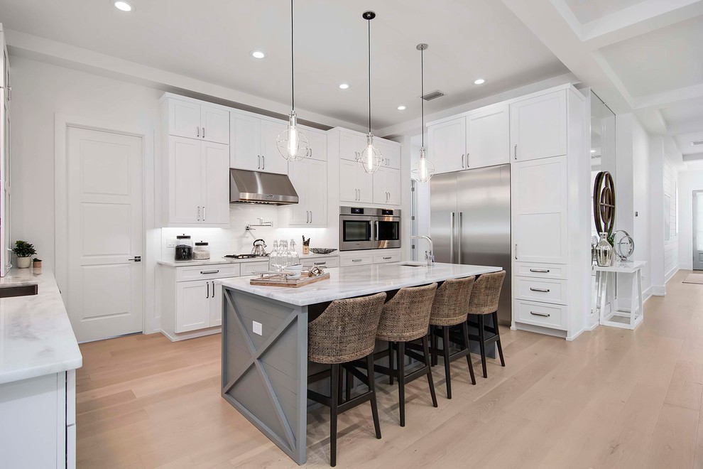 Large beach style l-shaped kitchen/diner in Orlando with a built-in sink, shaker cabinets, white cabinets, marble worktops, white splashback, porcelain splashback, stainless steel appliances, light hardwood flooring and an island.
