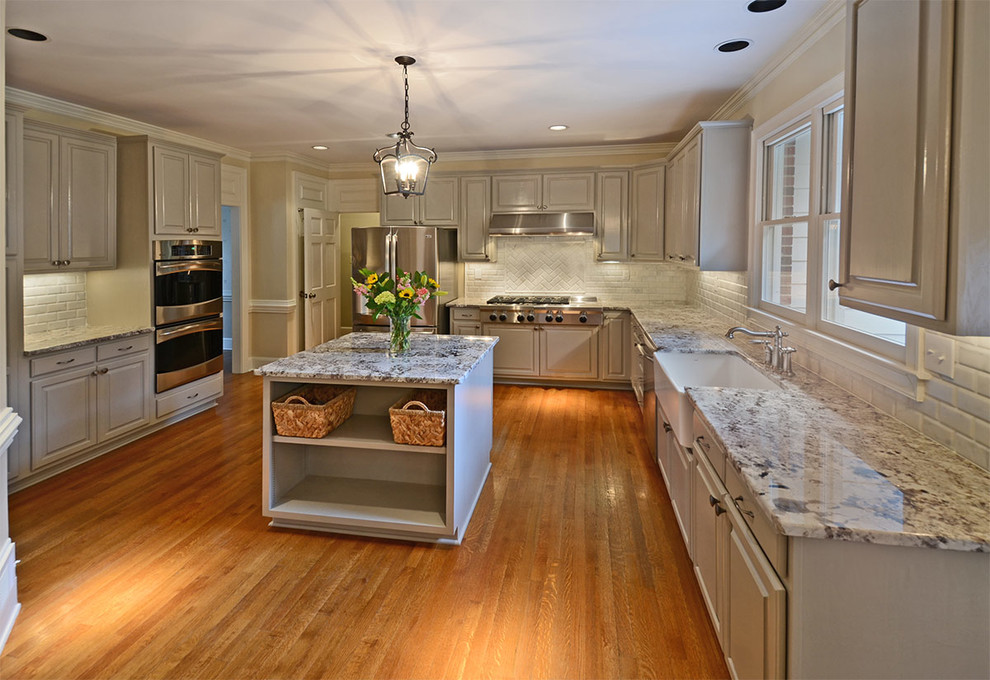 Large elegant u-shaped light wood floor eat-in kitchen photo in Other with a farmhouse sink, raised-panel cabinets, white cabinets, granite countertops, white backsplash, subway tile backsplash, stainless steel appliances and an island