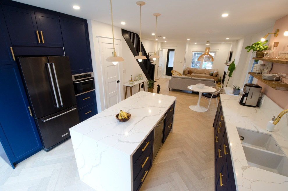 Modern inredning av ett mellanstort vit vitt kök, med en undermonterad diskho, skåp i shakerstil, blå skåp, vitt stänkskydd, stänkskydd i marmor, svarta vitvaror, mellanmörkt trägolv, en köksö, beiget golv och bänkskiva i kvarts