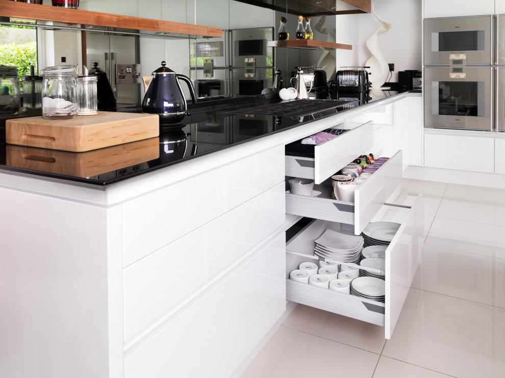 Inredning av ett modernt stort kök, med en dubbel diskho, släta luckor, granitbänkskiva, stänkskydd med metallisk yta, spegel som stänkskydd, rostfria vitvaror, klinkergolv i keramik, en köksö och vita skåp