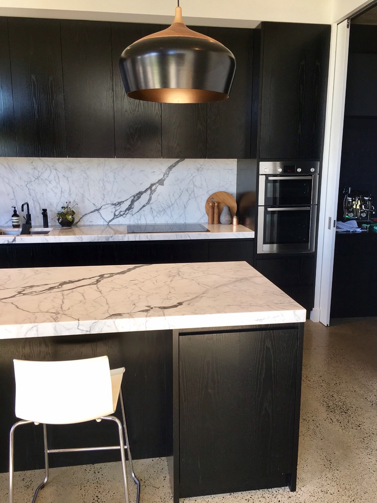 Modern inredning av ett mellanstort linjärt kök och matrum, med en undermonterad diskho, släta luckor, svarta skåp, marmorbänkskiva, stänkskydd i sten, rostfria vitvaror, kalkstensgolv och en köksö