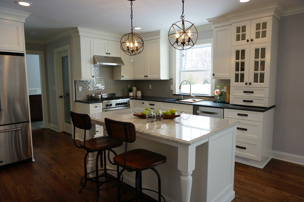 Exempel på ett mellanstort eklektiskt l-kök, med en enkel diskho, luckor med infälld panel, vita skåp, granitbänkskiva, grått stänkskydd, stänkskydd i glaskakel, rostfria vitvaror, mellanmörkt trägolv och en köksö