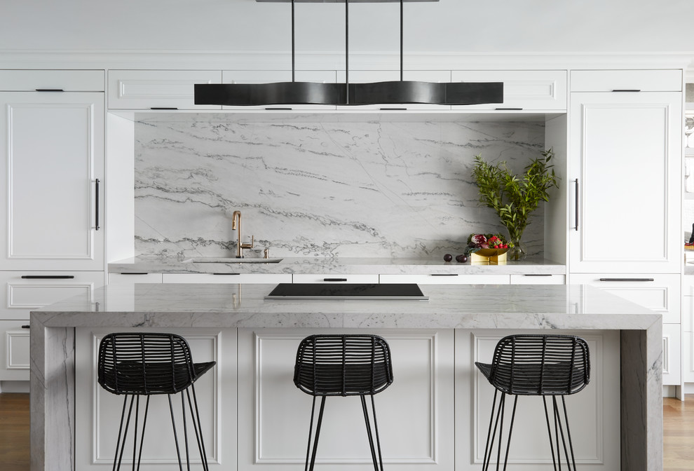 This is an example of a large contemporary galley kitchen/diner in Chicago with a submerged sink, white cabinets, quartz worktops, grey splashback, stone slab splashback, integrated appliances, medium hardwood flooring, an island, grey worktops, recessed-panel cabinets and brown floors.