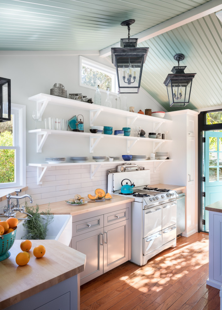 Enclosed kitchen - small coastal l-shaped medium tone wood floor, brown floor and vaulted ceiling enclosed kitchen idea in Los Angeles with a farmhouse sink, gray cabinets, wood countertops, white backsplash, ceramic backsplash, white appliances, no island, beige countertops and recessed-panel cabinets