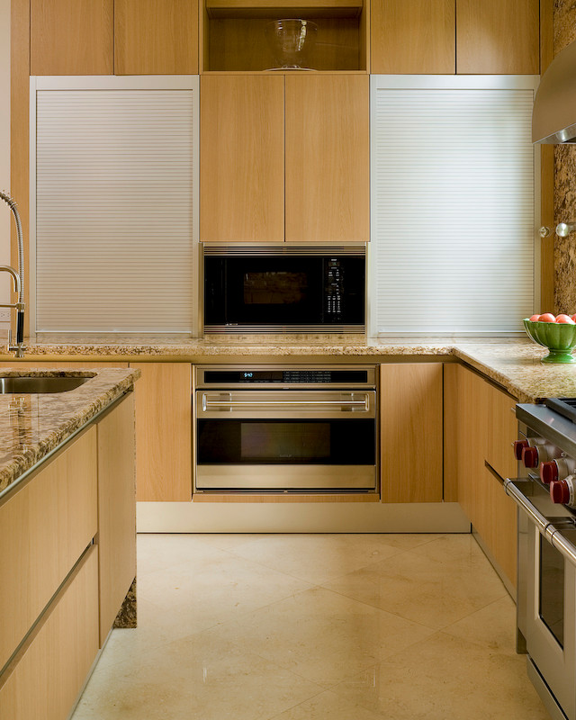 This is an example of a large modern u-shaped enclosed kitchen in Miami with a submerged sink, flat-panel cabinets, light wood cabinets, granite worktops, beige splashback, stone slab splashback, stainless steel appliances, marble flooring and an island.