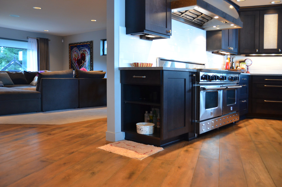 Example of a mid-sized transitional l-shaped dark wood floor and brown floor eat-in kitchen design in Seattle with shaker cabinets, black cabinets, concrete countertops, white backsplash, subway tile backsplash, stainless steel appliances and an island