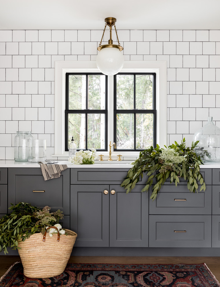 На фото: кухня в стиле кантри с врезной мойкой, фасадами в стиле шейкер, серыми фасадами, белым фартуком, белой столешницей и мойкой у окна