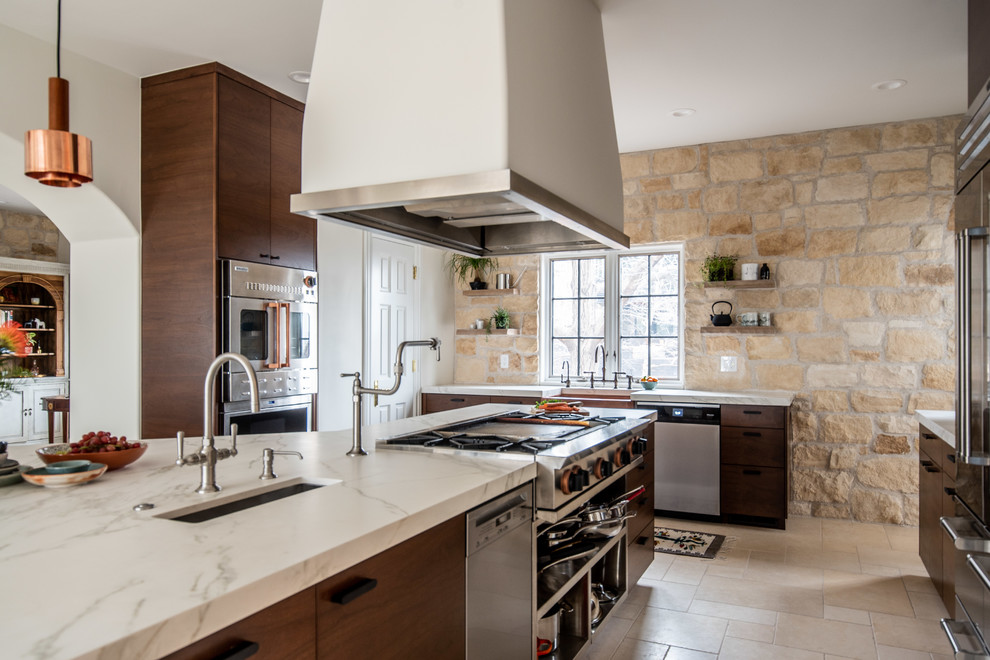 Inspiration for an expansive contemporary u-shaped kitchen pantry in Denver with a belfast sink, dark wood cabinets, beige splashback, stainless steel appliances, a breakfast bar, beige floors, flat-panel cabinets, marble worktops, stone tiled splashback, white worktops and limestone flooring.