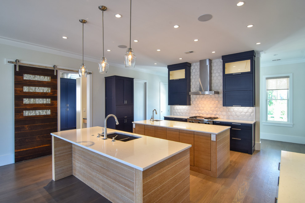 Large trendy galley medium tone wood floor and brown floor open concept kitchen photo in Charleston with a double-bowl sink, shaker cabinets, blue cabinets, solid surface countertops, white backsplash, ceramic backsplash, stainless steel appliances, two islands and white countertops