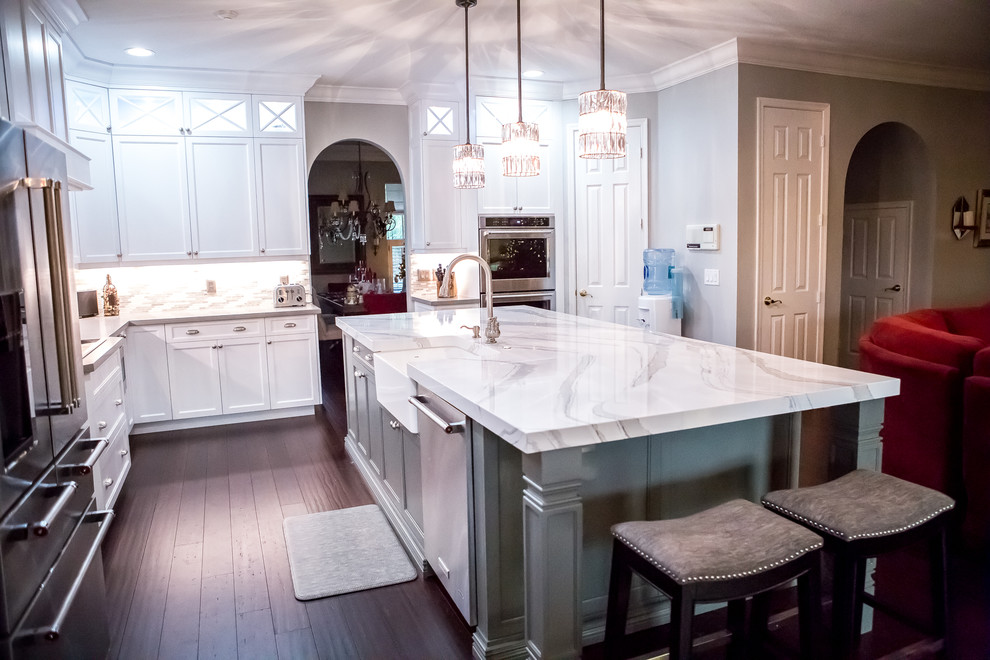 Klassisk inredning av ett stort vit vitt kök, med en rustik diskho, luckor med infälld panel, vita skåp, bänkskiva i kvartsit, flerfärgad stänkskydd, stänkskydd i stickkakel, rostfria vitvaror, mörkt trägolv, en köksö och brunt golv