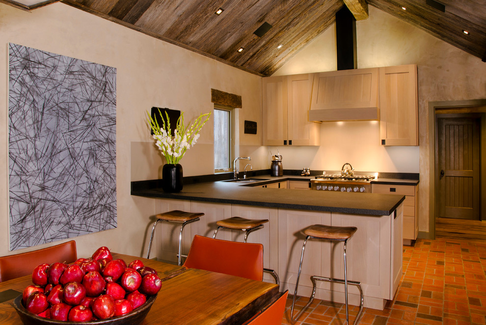Foto di una cucina design con lavello a doppia vasca, ante in stile shaker, ante in legno chiaro, elettrodomestici in acciaio inossidabile, pavimento in mattoni e penisola