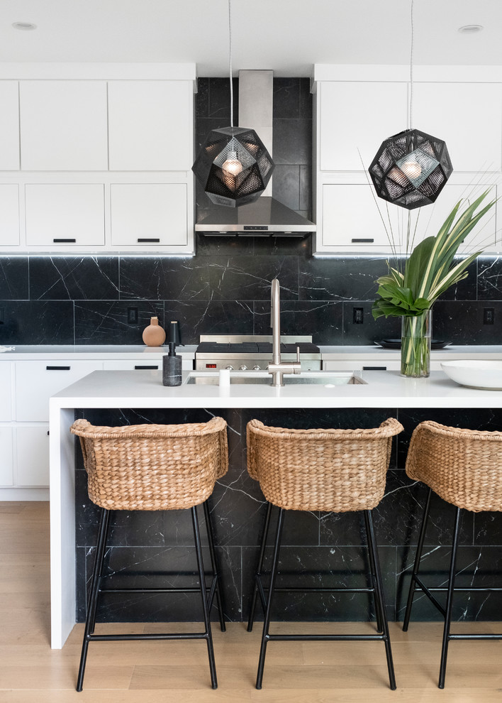 Foto på ett mellanstort maritimt vit kök, med en nedsänkt diskho, vita skåp, bänkskiva i kvarts, svart stänkskydd, stänkskydd i marmor, rostfria vitvaror, ljust trägolv, en köksö och brunt golv
