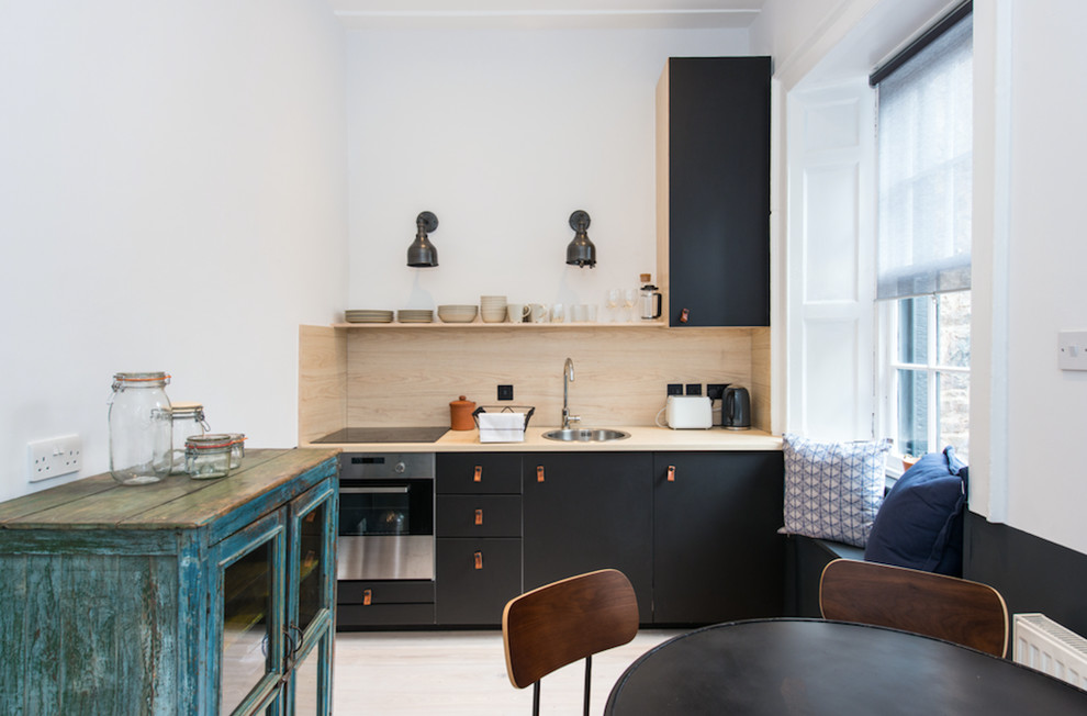 Foto på ett skandinaviskt linjärt kök och matrum, med en enkel diskho, släta luckor, svarta skåp, träbänkskiva, stänkskydd i trä, rostfria vitvaror, ljust trägolv och beiget golv