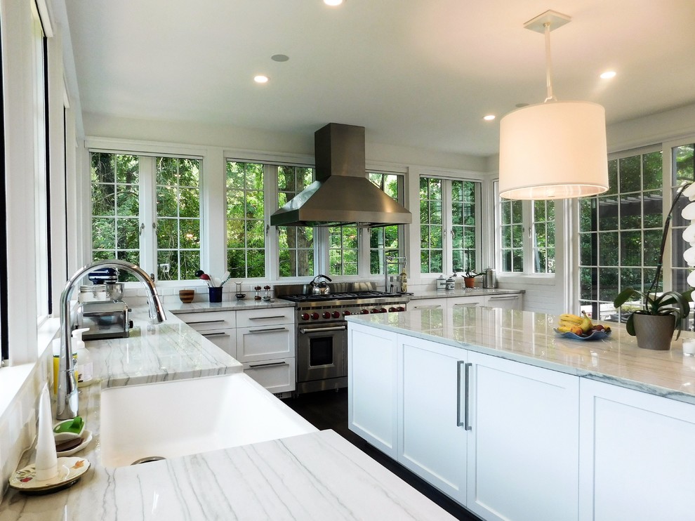 This is an example of a large traditional l-shaped kitchen/diner in Raleigh with a belfast sink, shaker cabinets, white cabinets, quartz worktops, window splashback, stainless steel appliances, dark hardwood flooring, an island and brown floors.