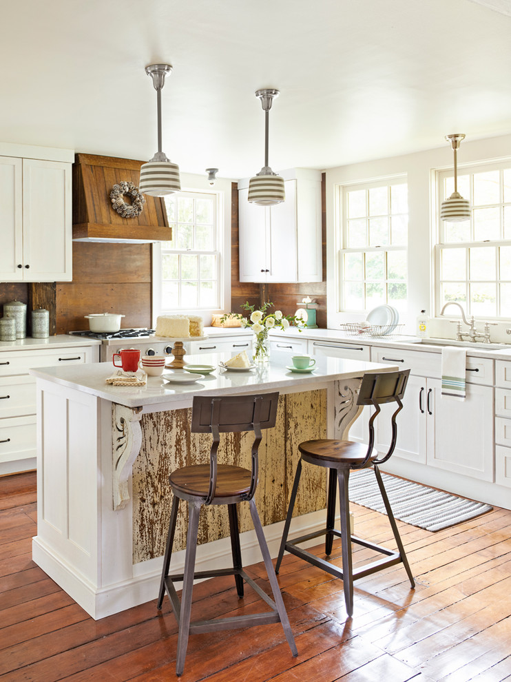 Example of a country l-shaped medium tone wood floor and brown floor kitchen design in Cleveland with an undermount sink, shaker cabinets, white cabinets, quartz countertops, brown backsplash, an island, wood backsplash and white countertops