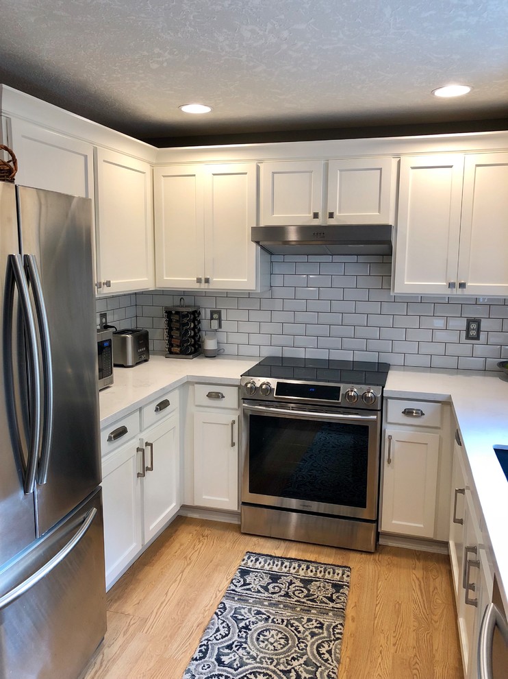 Exempel på ett avskilt, litet klassiskt vit vitt u-kök, med en undermonterad diskho, luckor med infälld panel, vita skåp, bänkskiva i kvarts, stänkskydd i tunnelbanekakel, rostfria vitvaror, ljust trägolv och gult golv
