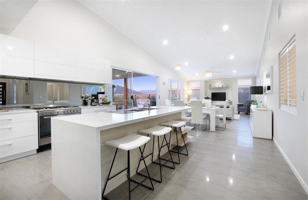 Photo of a medium sized modern galley open plan kitchen in Sunshine Coast with a double-bowl sink, white cabinets, engineered stone countertops, metallic splashback, mirror splashback, stainless steel appliances, porcelain flooring, an island and grey floors.